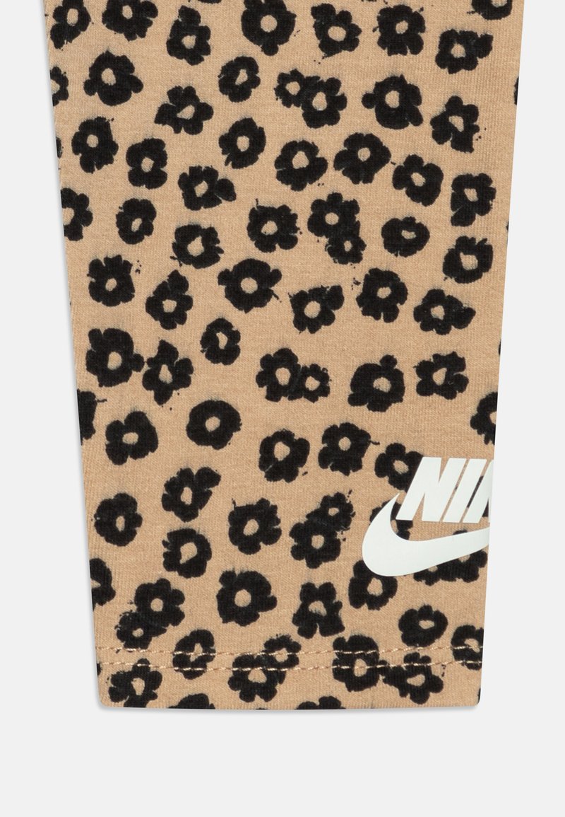 Beige Leggings aus weichem Material mit einem schwarzen Blumenmuster und weißem Nike-Logo. Die Stoffstruktur ist glatt. Fitting-Design.