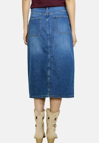 Denim midi krilo v modri barvi, s ravnim krojem, zadnjimi žepi in vidnimi šivi. Obuto z lahkimi svetlo rjavimi kavbojskimi čevlji s izrezljanimi detajli.