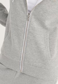 Felpa grigia con zip realizzata in tessuto morbido, con zip argentata, tasche a marsupio e polsini e orlo a costine. Design semplice.