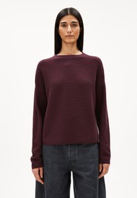 Bordeaux roter Pullover mit langen Ärmeln, rundem Halsausschnitt und Rippstruktur. Kombiniert mit locker sitzenden, dunkelgrauen Jeans. Einfaches und modernes Design.