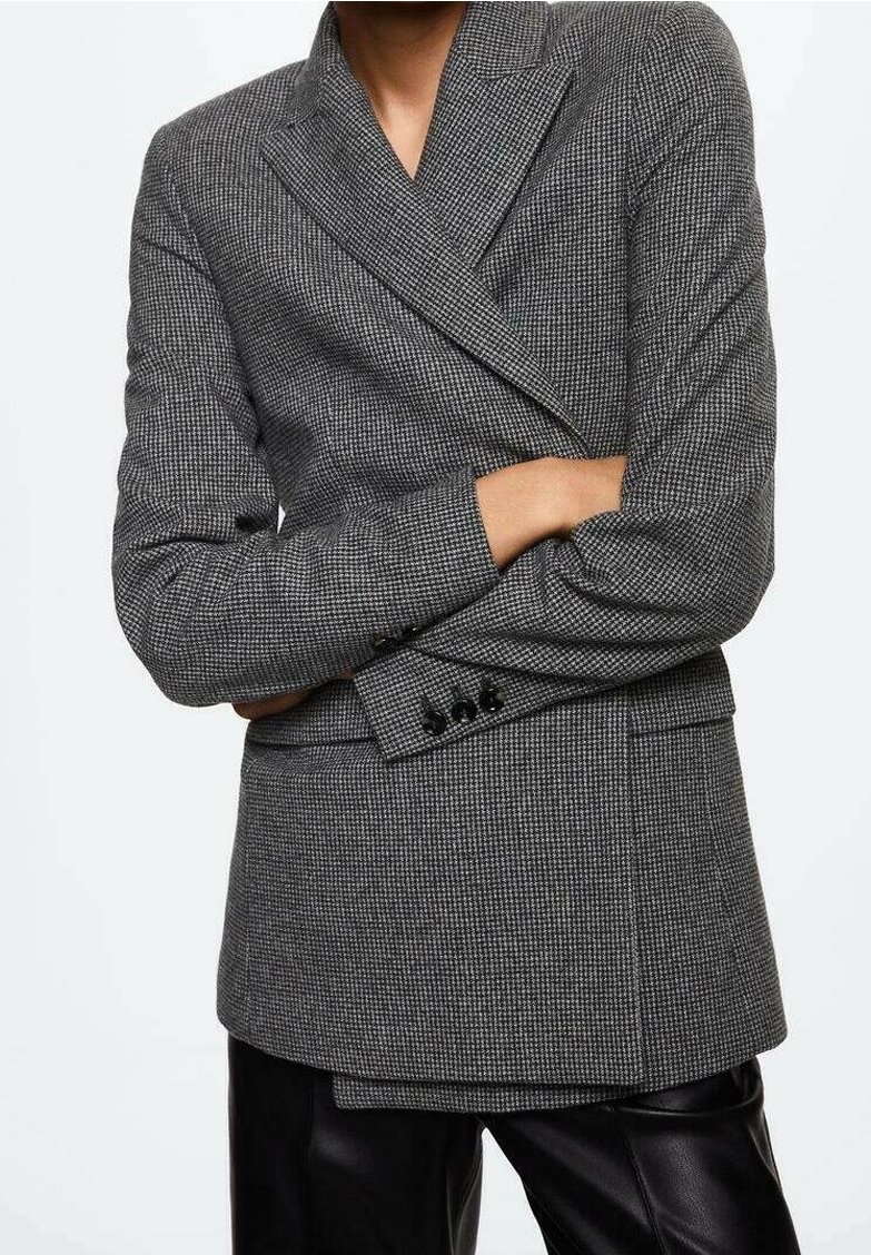 Blazer à carreaux gris en tissu texturé, présentant un devant croisé, de larges revers et des boutons noirs en accent, assorti à un pantalon sombre.