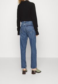 Hoch taillierte blaue Jeans aus Denim mit lockerer Passform, ausgestattet mit Gesäßtaschen und ausgefransten Säumen. Kombiniert mit einem schwarzen Langarmshirt und grünen Absatzsandalen.