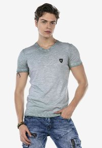 Grijze v-hals t-shirt met subtiele textuur, met korte mouwen en een klein zwart logo op de linkerborst. Gekocht met blauwe spijkerbroeken.