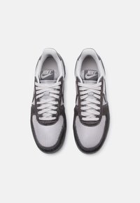 Et par grå og hvite Nike-sko med mesh- og semsket skinn-detaljer, hvite lisser og merkenavn på tungen sett ovenfra på en hvit bakgrunn.