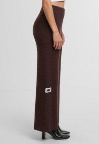 Hnědé pletené kalhoty rovného střihu s vysokým pasem a malou nášivkou na boku, zkombinované s černými špičatými podpatky.