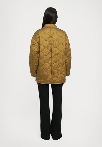 Kviltots zelta pūkains mētelis ar strukturētu apkakli un nolaižamām plecu daļām, kombinēts ar melniem platām biksēm, skatīts no aizmugures uz vienkārša fona.