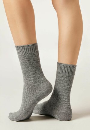 Chaussettes grises tricotées sur des jambes nues, avec des bords côtelés, un motif texturé et une longueur mi-mollet.