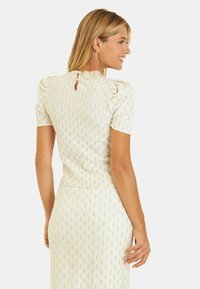 Jasna kremowa sukienka z teksturowanym diamentowym wzorem, krótkimi bufkami oraz detalem w kształcie łezki z tyłu. Dopasowany krój.