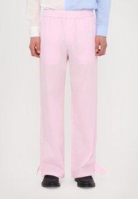 Calças pink xadrez com uma cintura elástica, corte descontraído e laços laterais na bainha. Combinadas com sapatos pretos e uma camisa multicolorida.