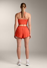 Czerwony sportowy crop top z krzyżującymi się ramiączkami i dopasowanymi szortami o wysokim stanie. Miękka tkanina, gładka powierzchnia i elastyczny pas.