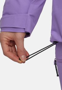 Paarse jas met opgerolde mouwen. Een hand trekt aan twee zwarte trekkoorden op de taille, wat de aanpasbare pasvorm toont.