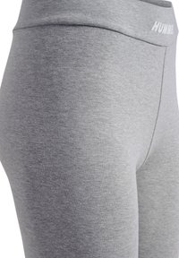 Grijze leggings van rekbare stof met een gladde textuur, met een hoge tailleband en een subtiele logo aan de voorkant.