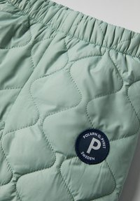 Vihreät päällystetyt shortsit, joissa on joustava vyötärö ja pyöreä sininen tarra, jossa on valkoinen "P" ja teksti "POLARN O. PYRET SWEDEN."