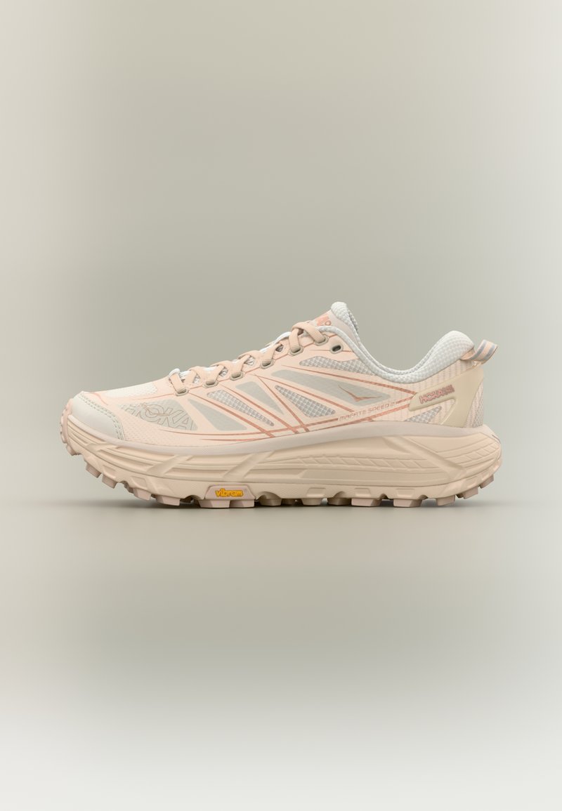 Zapatilla de trail running en rosa claro y blanco con suela acolchada y agarre Vibram, vista lateral sobre fondo neutro.