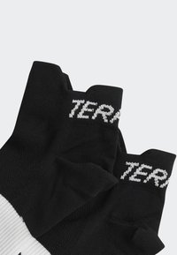 Guantes sin dedos de color negro hechos de tela de punto, con un logo blanco en el puño y un patrón texturizado en la palma para mayor agarre.