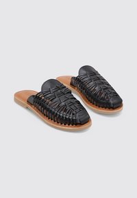 Sandalias deslizantes de cuero trenzado negro con diseño de punta abierta, que presentan una plantilla marrón y una suela plana para mayor comodidad.