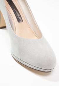 Chaussure pour femme en daim gris clair, à talon bas, bout arrondi et doublure intérieure beige sur fond blanc.
