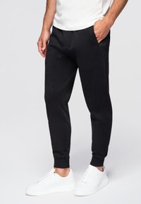 Svarta joggingbyxor i mjukt material, med en tapered design, sidofickor och ribbade muddresårer. Matchas med vita sneakers.