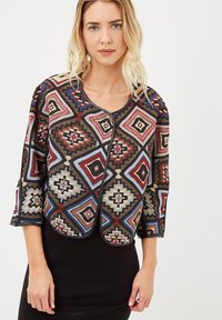 Chaqueta corta con un diseño geométrico en tonos rojos, azules y beiges, con mangas de tres cuartos y un cuello redondeado.