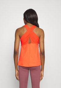 Rode sportieve tanktop met een kruisrugontwerp, voorzien van een uitsnijding in de vorm van een sleutelgat en van een soepele, rekbare stof. Gecombineerd met donkerpaarse leggings.
