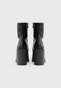 Schwarze Leder-Stiefeletten mit strukturiertem Finish, ausgestattet mit einem hohen Blockabsatz und einem Reißverschluss hinten. Einfaches, elegantes Design.