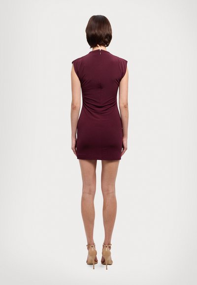 Κοντό μωβ φόρεμα με εφαρμοστή γραμμή, υφασμάτινη υφή και φερμουάρ στην πλάτη. Φοριέται με γυμνά ψηλοτάκουνα παπούτσια.