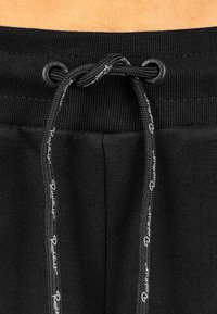 Zwarte elastische tailleband met een trekkoord en witte logo-detaillering. Zachte stof met een gladde textuur en vlakke stiksels.