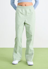 Pantalones jogger ligeros de color verde claro, con cintura elástica y un pequeño logo blanco. Textura suave y diseño de pierna recta.