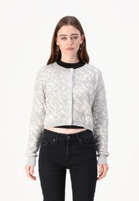 Grå, kort cardigan med teksturert mønster, fem knapper og ribbestrikkede mansjetter. Kombinert med svarte høy midje jeans.
