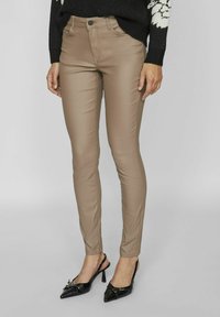 Bež hlače slim fit iz raztegljivega materiala z gladko teksturo, z običajnim pasom in sprednjimi žepi. Usklajene z črnimi petami.