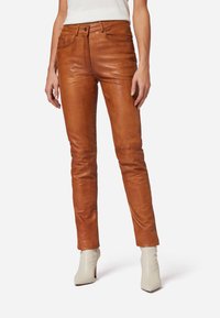 Braune Lederhosen mit passgenauer Silhouette, klassischem Fünf-Taschen-Stil und glatter Textur. Getragen mit weißen Absatzstiefeln.