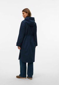 Lång marinblå regnkappa med huva, insvängd midja och sidofickor. Slät textur med en minimalistisk design utan synliga detaljer.