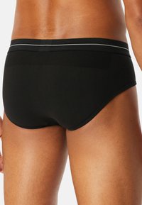 Svarta herrunderkläder i briefs-stil med en slät yta, en figurnära passform och ett kontrasterande grått midjeband. Designen är enkel och funktionell.