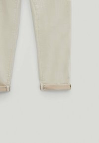 Pantalons beige clair en coton, présentant une coupe droite avec des ourlets repliés et une texture subtile, adaptés pour un usage décontracté.