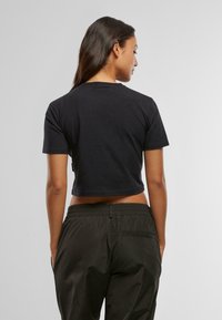 Musta lyhythihainen crop-top, jossa pyöreä kaula-aukko, pehmeää puuvillamateriaalia, yhdistettynä tummaan rentoon housumalliin. Yksinkertainen ja minimalistinen muotoilu.