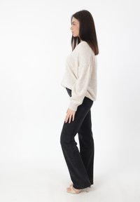 Maglione a maglia crema con una vestibilità rilassata, abbinato a jeans flare neri a vita alta. Modella che indossa sandali con tacco beige, in piedi di profilo.