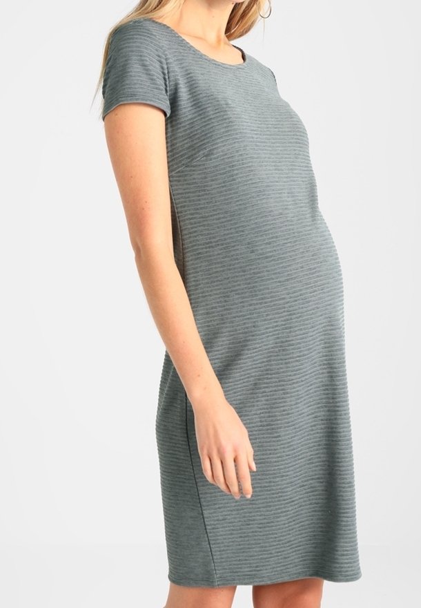 Femme portant une robe de maternité grise, à manches courtes, longueur genoux avec de fines rayures horizontales, se tenant devant un fond clair uni.