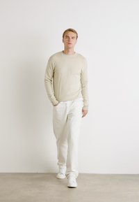 Maglione beige chiaro con collo a giro, abbinato a pantaloni bianchi leggermente larghi. Scarpe da ginnastica bianche completano l'outfit. Texture liscia.