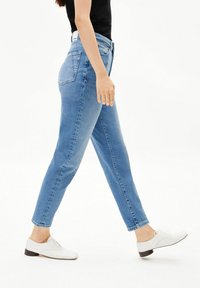 Lichtblauwe denim jeans met een slim fit, hoge taille en vijf zakken. Gecombineerd met witte veterschoenen en een zwart topje.
