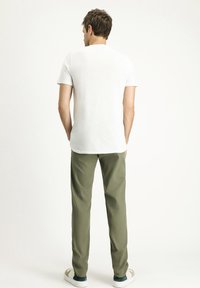 Camiseta blanca de manga corta combinada con pantalones verde oliva y zapatillas blancas, con un diseño simple y un ajuste holgado.