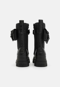 Bottines noires avec un dessus en tissu texturé, semelle en caoutchouc épaisse, fermeture éclair et poches latérales. Logo "Buffalo" sur le talon.