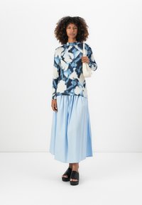 Blauw en witte tie-dye longsleeve top, gecombineerd met een lichtblauwe, geplooide maxi rok. Draagt zwarte plateau sandalen. Eenvoudige handtas.