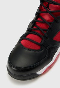 Sorte lær og rød mesh sneaker med en teksturert finish, med sorte snørebånd og en hvit mellomsåle med en rød gjennomsiktig yttersåle.