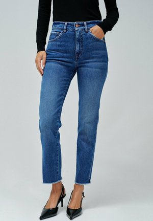 Vaqueros de mezclilla azul de cintura alta con corte recto, dobladillo deshilachado y bolsillos. Llevados con tacones negros de puntera puntiaguda.