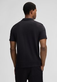 Schwarz kurzärmliges Polohemd aus strukturiertem Stoff, mit klassischem Kragen und geradem Saum, das ein minimalistisches Design zeigt.