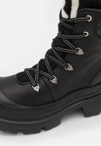 Bota de cuero negro con acabado texturizado, forro de lana en el caña, herrajes plateados y suela de goma con surcos profundos para mayor tracción.