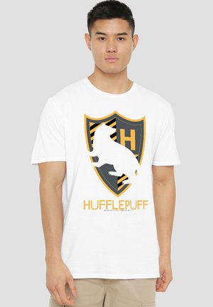 Young man wearing a white t-shirt with a yellow and black Hufflepuff crest featuring a badger and the word "HUFFLEPUFF."