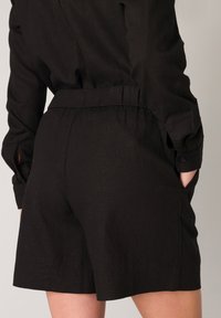 Zwarte linnen shorts met een ontspannen pasvorm. Kenmerken zijn een elastische tailleband en zijzakken; de textuur lijkt glad en lichtgewicht.