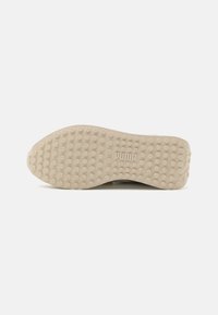 Semelle en caoutchouc beige clair avec un motif de grip circulaire texturé. Elle présente un logo en relief et des bords lisses pour un design épuré.