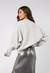 Szürke túlszabott pulóver lógó vállakkal, ezüst flitteres szoknyával párosítva, melynek combig érő hasítása rétegezett megjelenést kölcsönöz.